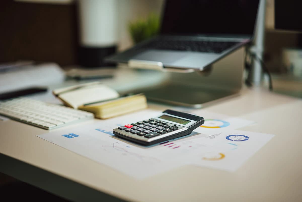 Small business seller calculating Etsy product pricing with a notebook, calculator, and product samples